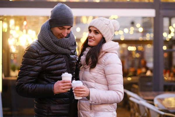 Feliz pareja romántica vistiendo ropa de abrigo disfrutando pasar tiempo juntos en una cita en la calle de la noche cerca de un café al aire libre en Navidad — Foto de Stock