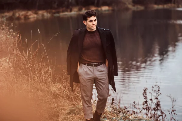 Ein hübscher junger Mann steht in der Nähe eines Sees im herbstlichen Wald. — Stockfoto