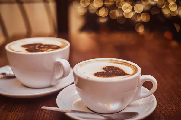 Två koppar kaffe med konst på trä bordet i ett kafé, sudda bakgrunden med bokeh effekt — Stockfoto