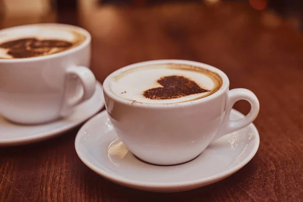 Två koppar kaffe med konst på trä bordet i ett kafé, sudda bakgrunden med bokeh effekt — Stockfoto