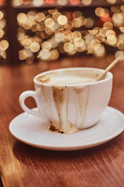 Cup with spilled coffee on the wooden table in a coffee shop, blur background with bokeh effect — Stock Photo, Image