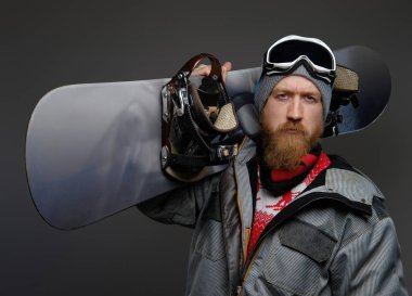 Karanlık bir arka plan üzerinde izole ciddi bir göz ile a fotoğraf makinesi vasıl görünen emin adam tam bir ekipman snowboard omzunda, holding giyen kırmızı sakallı.