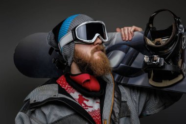 Karanlık bir arka plan üzerinde izole onun omzuna bir snowboard tutan bir tam ekipmanlı giyen kırmızı sakallı acımasız adam.