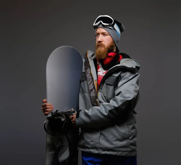 一个红头发的胡须男子穿着全副武装的设备拿着滑雪板, 望着外看, 被隔离在黑暗的背景中的肖像. — 图库照片