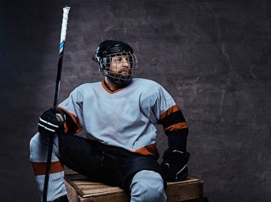 Tam giyen sakallı hokey oyuncusu portresi spor malzemeleri ahşap palet üzerinde otururken bir hokey sopası holding. 