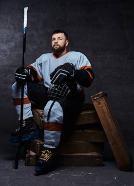 Tam giyen sakallı hokey oyuncusu portresi spor malzemeleri ahşap palet üzerinde otururken bir hokey sopası ve kask holding. 