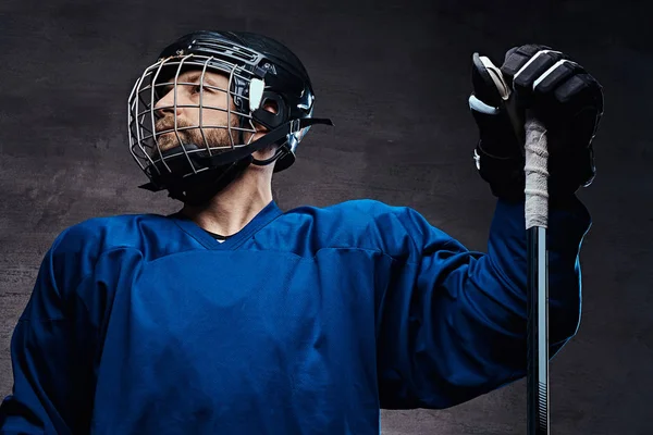 Portrait of a bearded ice-hockey player in a blue sportswear with gaming stick. Studio shot. — Stock Photo, Image