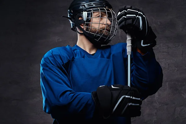 Ritratto di un giocatore di hockey su ghiaccio barbuto in abbigliamento sportivo blu con bastone da gioco. Studio girato . — Foto Stock