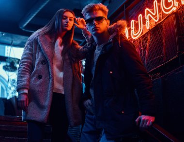 Merdiven yeraltı gece kulübü için arka plan arkadan aydınlatmalı tabela Instalar sıcak giysiler giyen genç bir şık çift