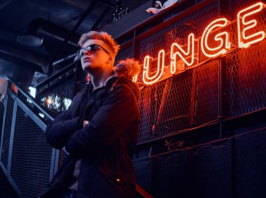 Kürk başlık ile bir kat ve kollarını ile güneş gözlüğü giyen genç bir kendine güvenen adam ayakta geçti yeraltı gece kulübü için merdiven, arka plan arkadan aydınlatmalı tabela