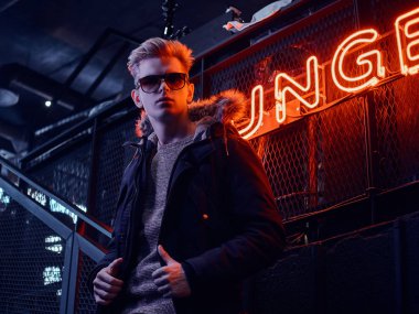 Kürk başlık ve yeraltı gece kulübü için merdiven, arka plan arkadan aydınlatmalı tabela Instalar güneş gözlüğü takan paltoyla kendine güvenen genç bir adam