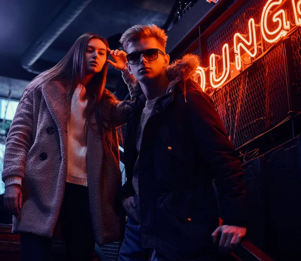 Modny ubrany Młoda para stojący na schody do podziemnego klubu nocnego, szyld podświetlany w tle — Zdjęcie stockowe