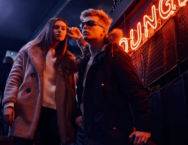 Модная молодая пара, стоящая на лестнице в подземный ночной клуб, на заднем плане вывеска с подсветкой — стоковое фото