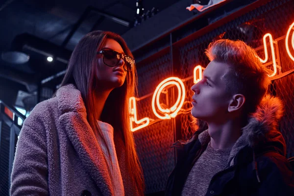 Młoda para stylowe nosić ciepłe ubrania stojący w kawiarni z wnętrza przemysłowe, szyld podświetlany w tle — Zdjęcie stockowe