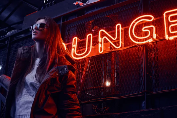 Joven chica elegante con una sudadera con capucha y gafas de sol de pie en las escaleras en la discoteca subterránea con interior industrial —  Fotos de Stock