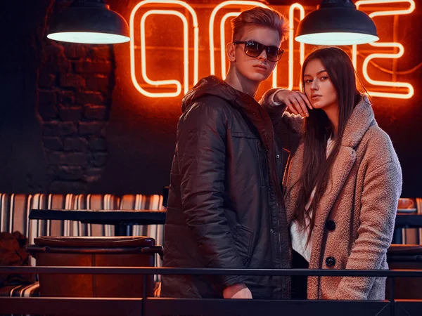 Atractiva pareja joven usando ropa elegante posando juntos en un café con interior industrial —  Fotos de Stock