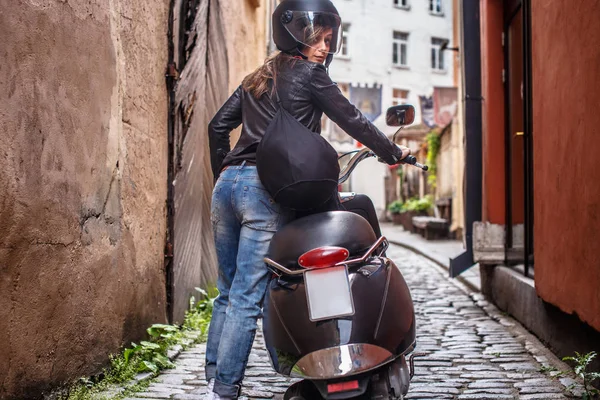 Bir kız ile bir scooter Letonya eski dar sokaklar boyunca yürüyüş arkadan görünüm. — Stok fotoğraf
