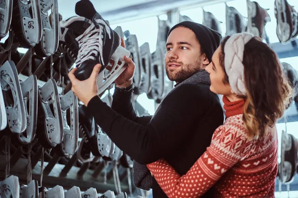 Junges Paar in warmer Kleidung, das in der Nähe des Gepäckträgers mit vielen Paar Schlittschuhe steht und seine Größe auswählt — Stockfoto