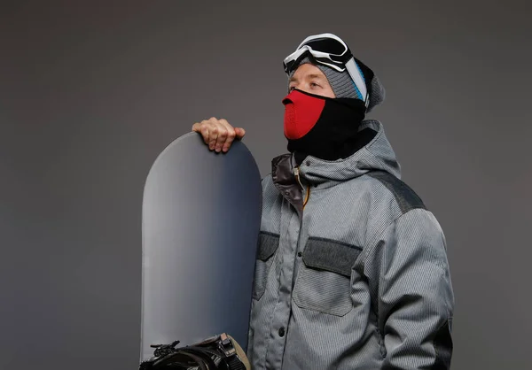 Portrait of a snowboarder wearing full protective equipment for extreme snowboarding posing with snowboard at a studio, isolated on a dark background. — Stock Photo, Image