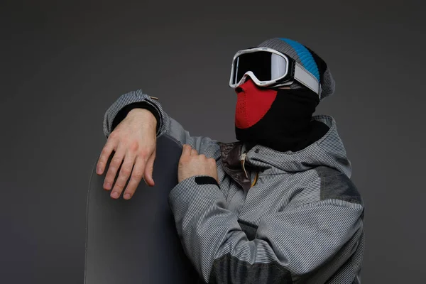 Portrait of a snowboarder wearing full protective equipment for extreme snowboarding posing with snowboard at a studio, isolated on a dark background. — Stock Photo, Image