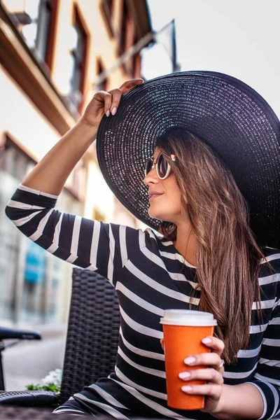 Портрет молодої модної жінки в сонцезахисних окулярах і стильному капелюсі, що сидить у літньому вуличному кафе . — стокове фото