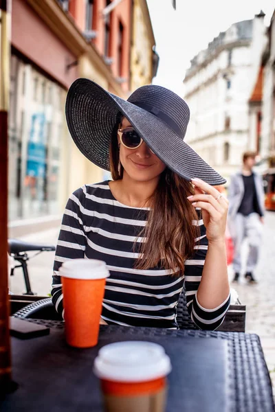 Porträt einer jungen modischen Frau mit Sonnenbrille und stylischem Hut in einem sommerlichen Straßencafé. — Stockfoto