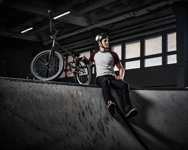 Bmx гонщик розслабляється після тренування трюків з велосипедом в скейтпарку в приміщенні — стокове фото