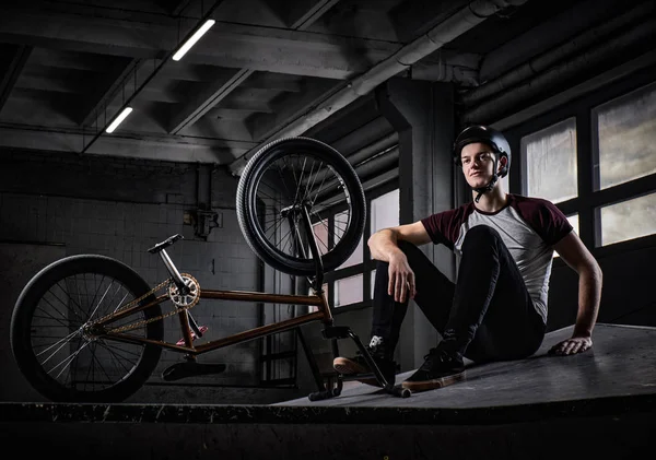 Bmx jinete relajante después de practicar trucos con su bicicleta en un skatepark en el interior — Foto de Stock