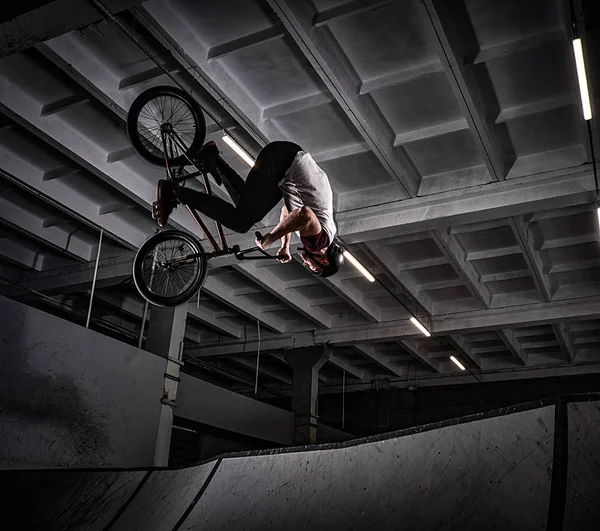 Joven con BMX haciendo trucos en skatepark en interiores — Foto de Stock