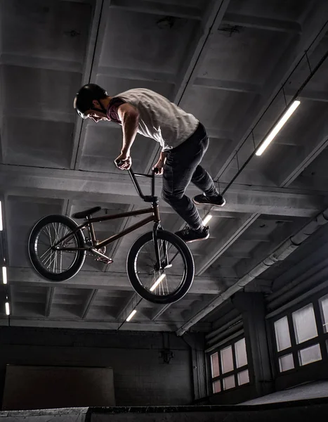 Молодий BMX робить божевільні трюки на своєму велосипеді в скейтпарку в приміщенні . — стокове фото
