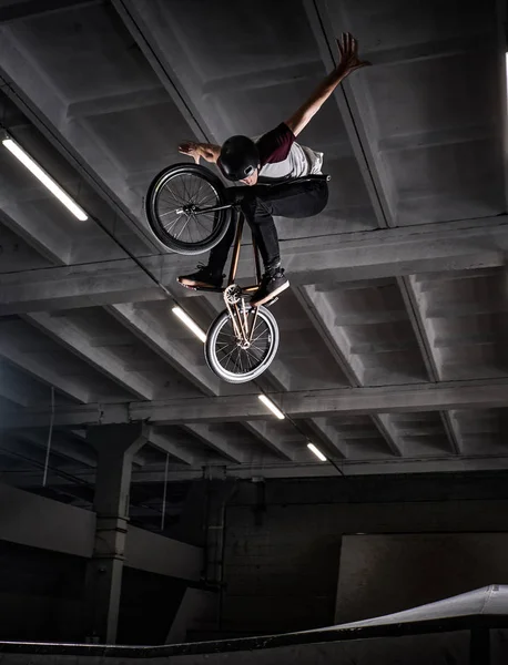 Молодий BMX робить божевільні трюки на своєму велосипеді в скейтпарку в приміщенні . — стокове фото