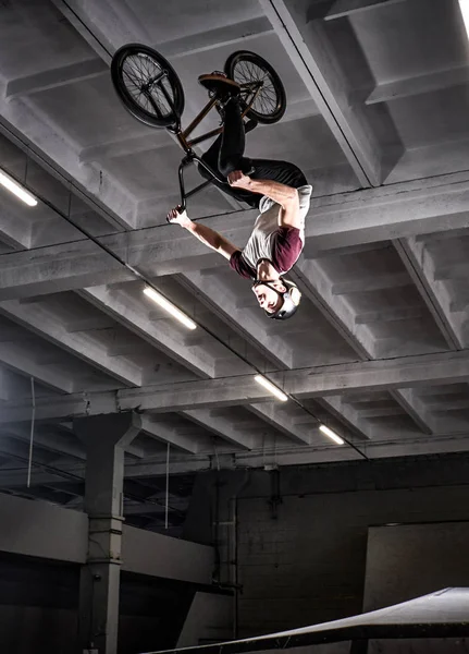 Jovem BMX fazendo truques loucos em sua bicicleta no skatepark dentro de casa . — Fotografia de Stock