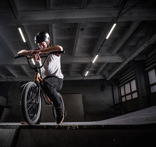 Adolescente BMX cavaleiro sentado em sua bicicleta em um parque de skate dentro de casa — Fotografia de Stock