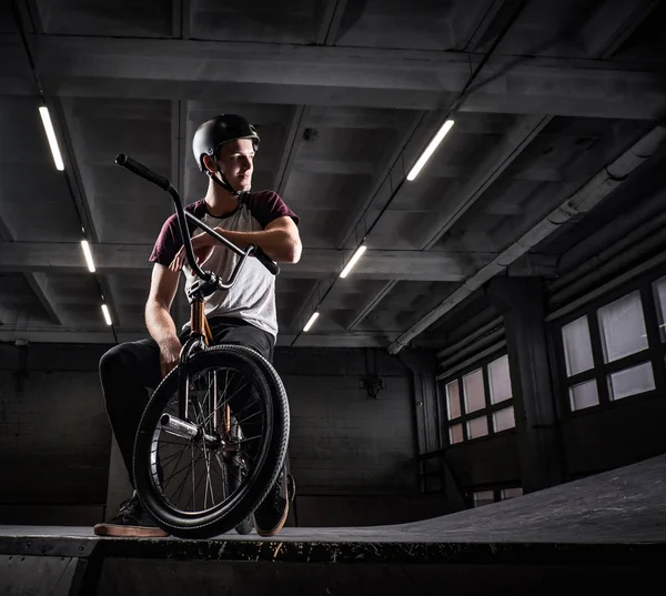 Joven jinete BMX sentado en su bicicleta en un parque de skate en el interior — Foto de Stock
