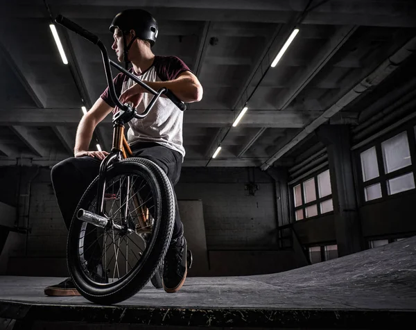 Підліток BMX вершник сидить на своєму велосипеді в скейтпарку в приміщенні — стокове фото