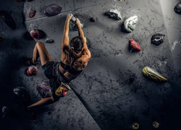 Mujer joven usando ropa deportiva practicando escalada en roca en una pared interior — Foto de Stock