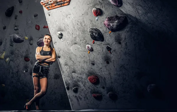 Porträt einer fröhlichen Bergsteigerin, die sich an eine Boulderwand in der Turnhalle lehnt. — Stockfoto