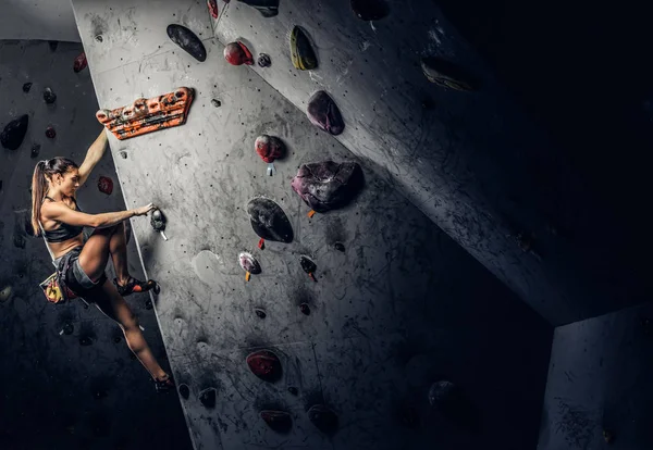 Mujer joven usando ropa deportiva practicando escalada en roca en una pared interior — Foto de Stock