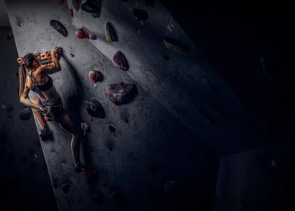 Mujer joven usando ropa deportiva practicando escalada en roca en una pared interior —  Fotos de Stock