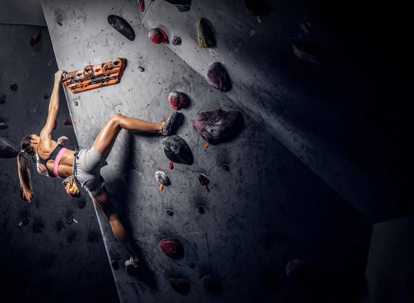 Mujer joven usando ropa deportiva practicando escalada en roca en una pared interior — Foto de Stock