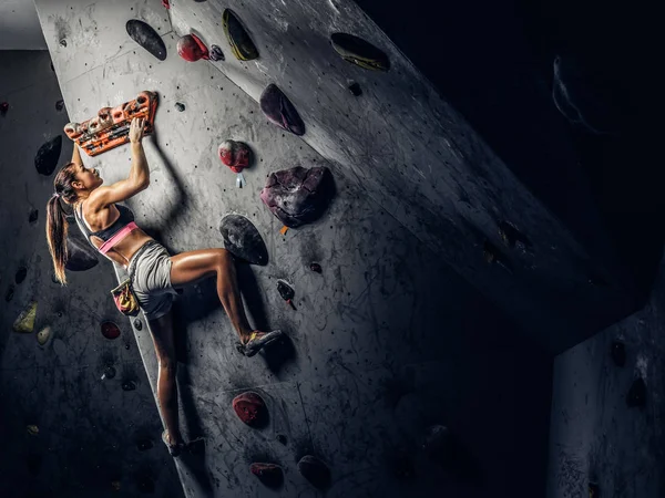 Mujer joven usando ropa deportiva practicando escalada en roca en una pared interior — Foto de Stock