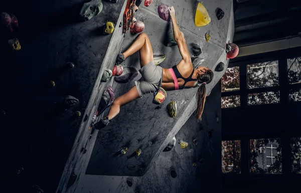 Deportiva mujer escalando roca artificial en interiores . — Foto de Stock