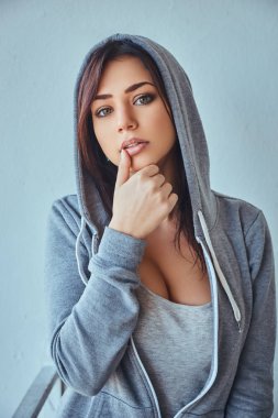 Güzel genç yetişkin esmer kadın yüzünü dokunaklı ve bir kameraya bakarak gri kapüşonlu.