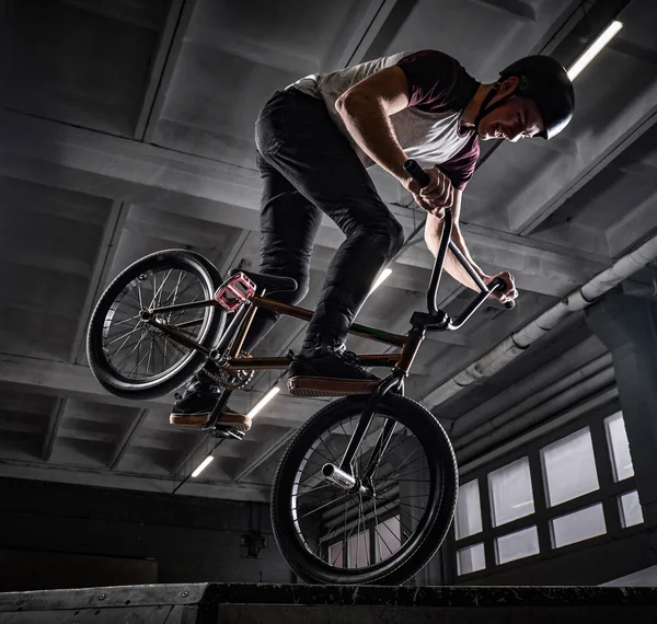 Joven con BMX haciendo trucos en skatepark en interiores — Foto de Stock