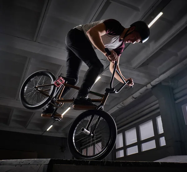 Joven con BMX haciendo trucos en skatepark en interiores — Foto de Stock