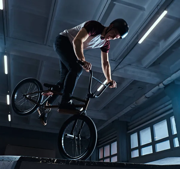 Молодий чоловік з BMX виконує трюки в скейтпарку в приміщенні — стокове фото