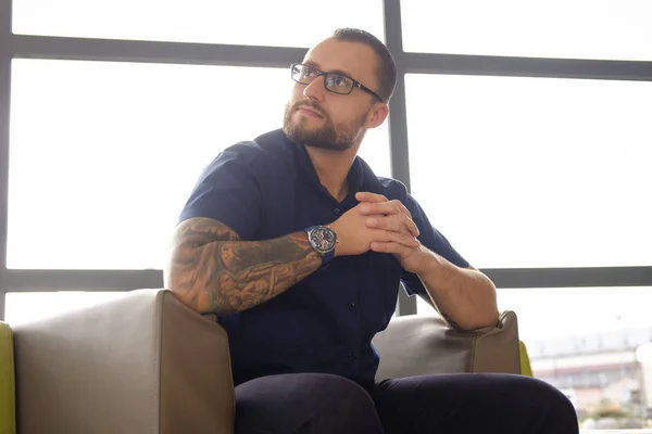 Zamyšlený podnikatel oblečený v modré košili, sedící na gauči v kanceláři — Stock fotografie