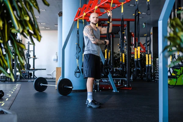 Wytatuowany mężczyzna sportowiec trzyma fitness zawieszenie liny w siłowni — Zdjęcie stockowe