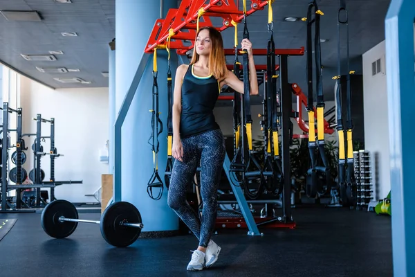 Menina alegre vestindo sportswear segurando uma suspensão tiras de fitness no ginásio — Fotografia de Stock