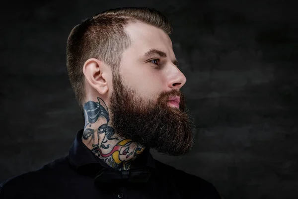 Retrato de perfil de un expresivo hombre barbudo con tatuajes en el cuello, aislado sobre un fondo oscuro . — Foto de Stock